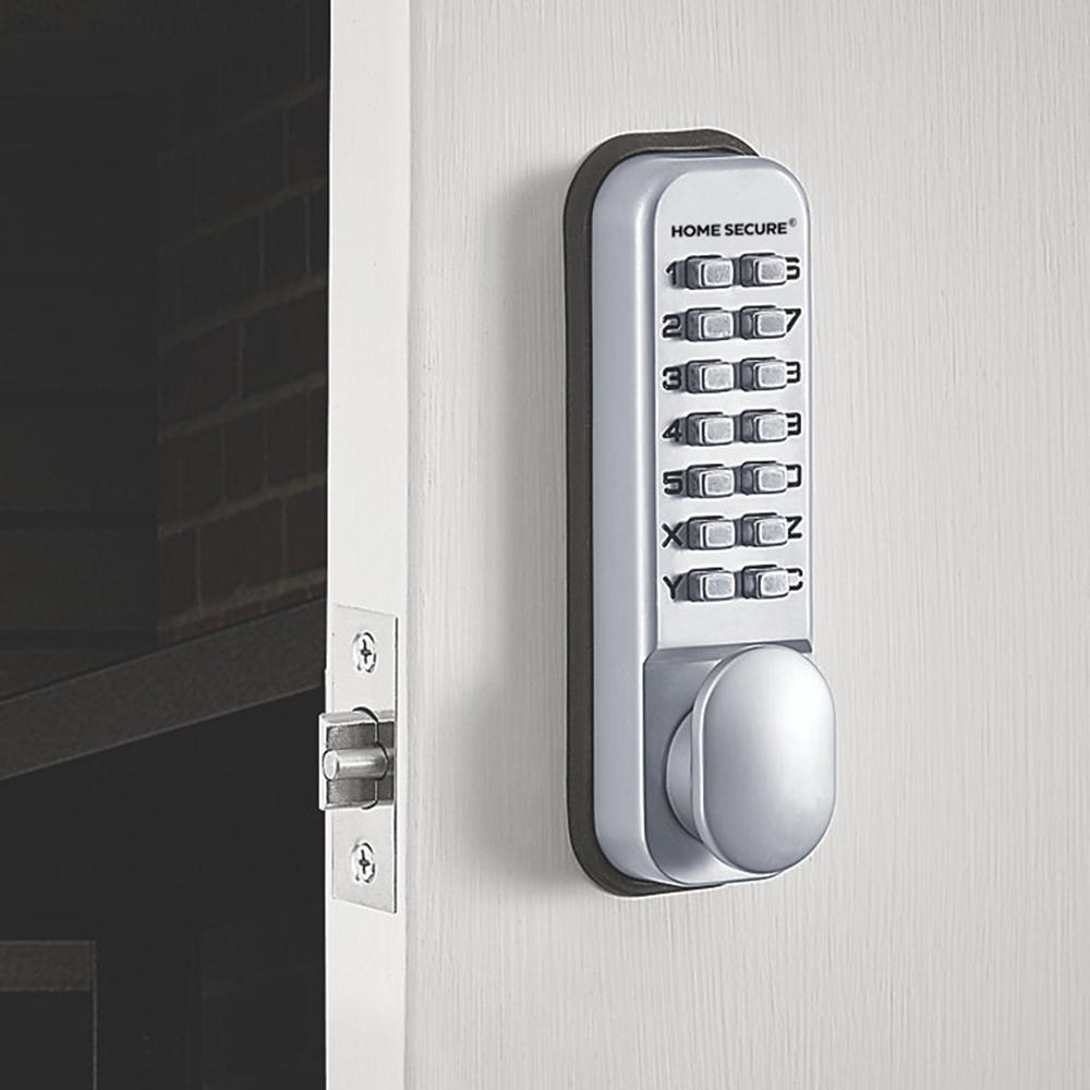 Digital mechanical door lock by Home Secure installed on a white door. The lock features a silver keypad with numbered push buttons (0–9) and a thumb turn at the bottom. The latch is visible on the door edge, aligned with the strike plate on the door frame