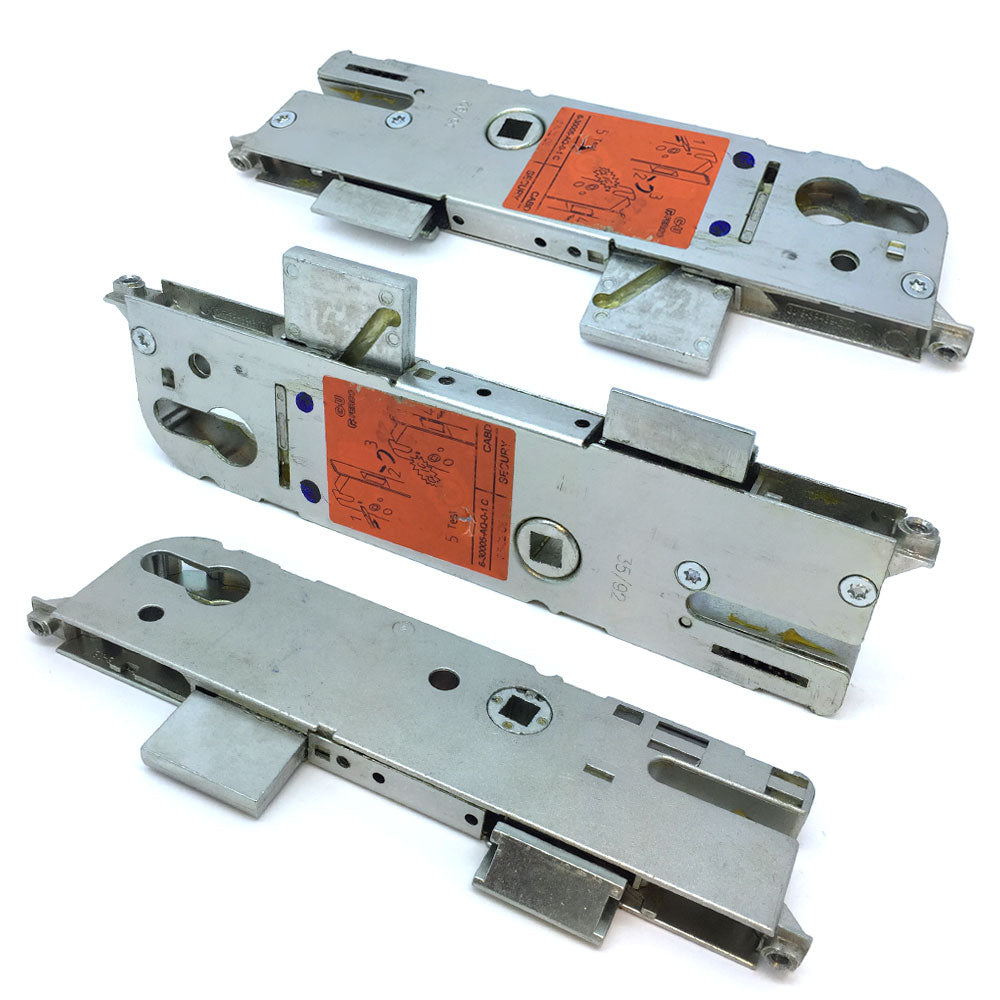 Three metal door lock gearboxes laid out on a white surface, with varying amounts of visible dirt and markings.