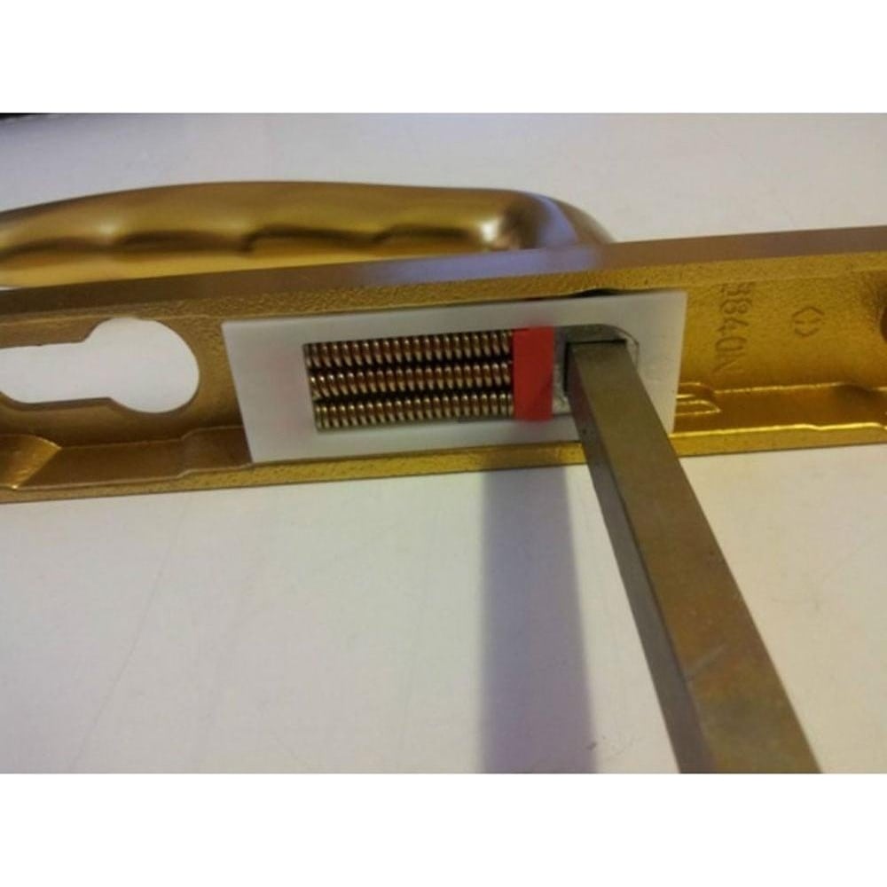 Close-up of a gold-colored UPVC door handle with a screwdriver inserted, showing the replacement spring mechanism inside the handle.