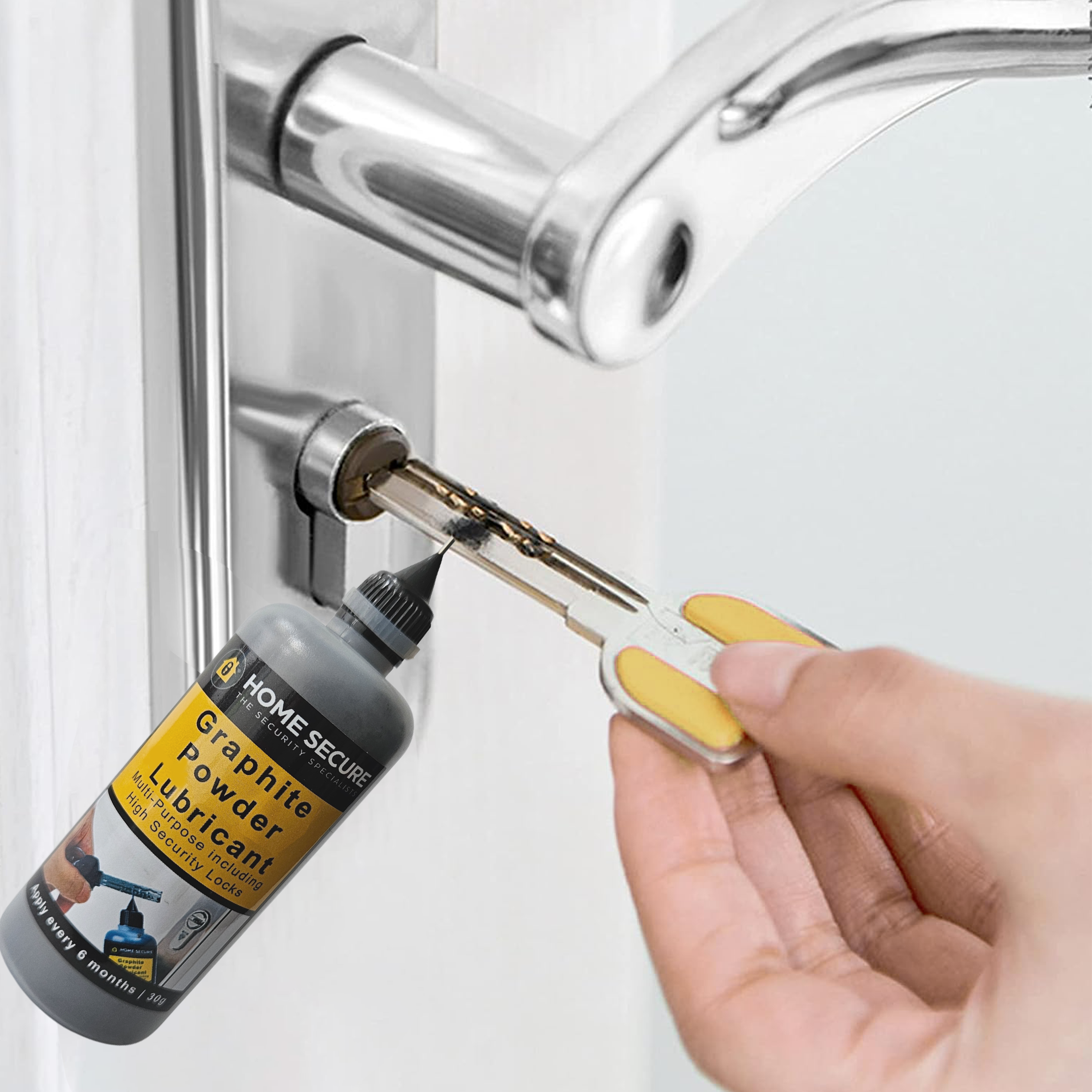 A hand holding a key inserted into a door lock, with a bottle of Home Secure Graphite Powder Lubricant nearby, implying the lubricant is being applied to the lock for smoother operation