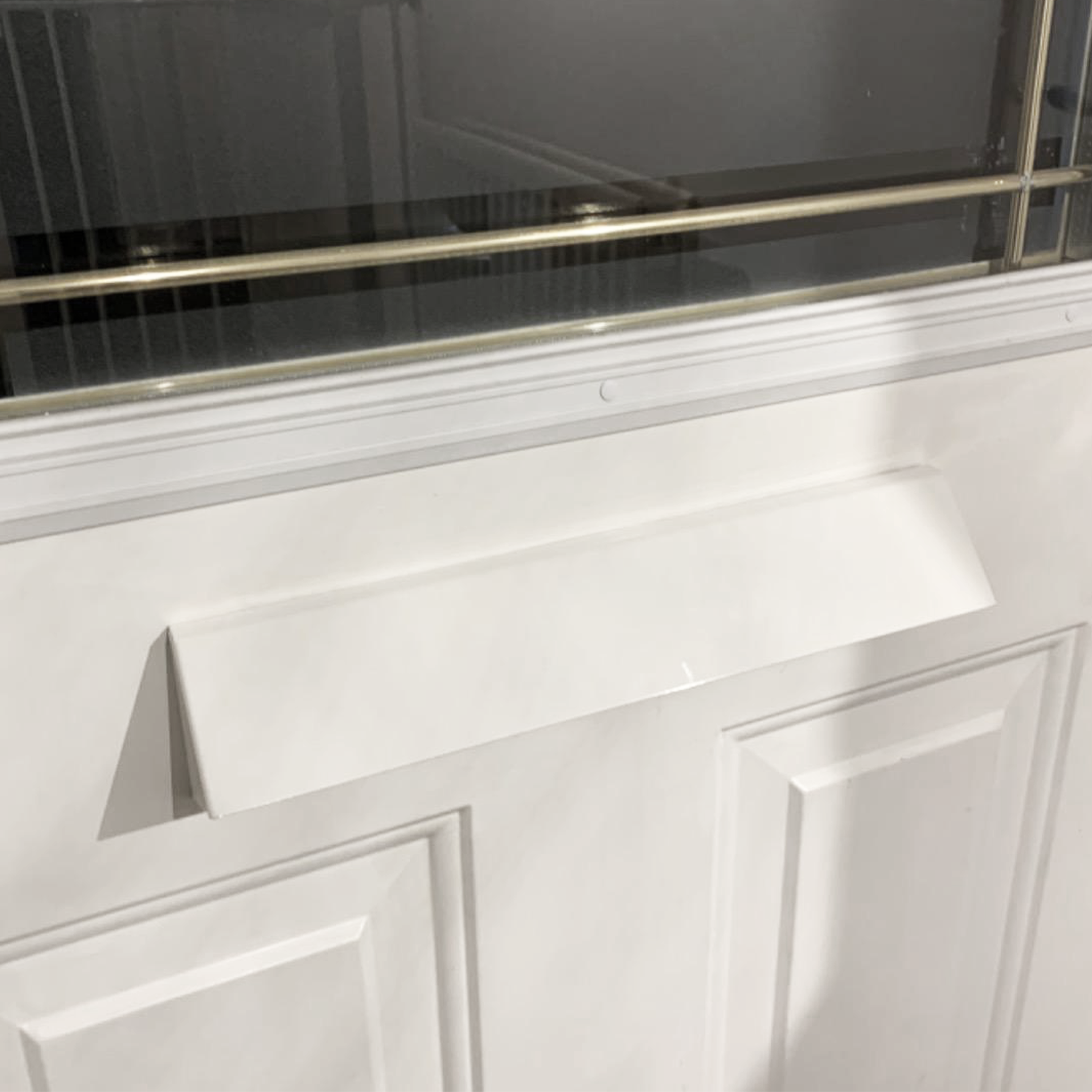 Close-up of a white front door with a rectangular mail slot cover installed beneath a decorative glass panel. The mail slot flap is angled outward, matching the door's white color and clean design