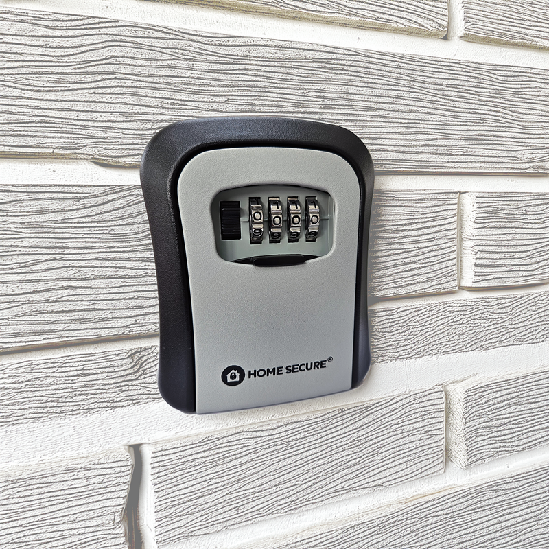 Wall-mounted Home Secure® outdoor key safe box attached to an exterior brick wall. The safe features a black and grey design with a 4-digit combination lock on the front
