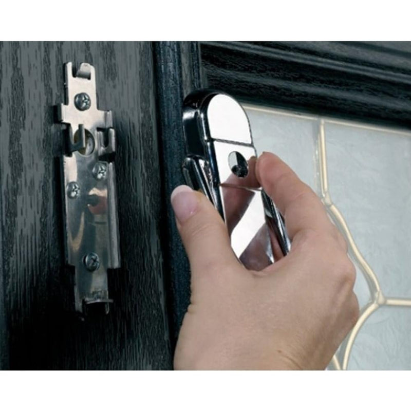A close-up image of a person’s hand attaching a shiny chrome door knocker to a black front door. The mounting plate is already fixed to the door, and the knocker is being aligned and secured onto it. The door features a decorative glass panel with a textured pattern.
