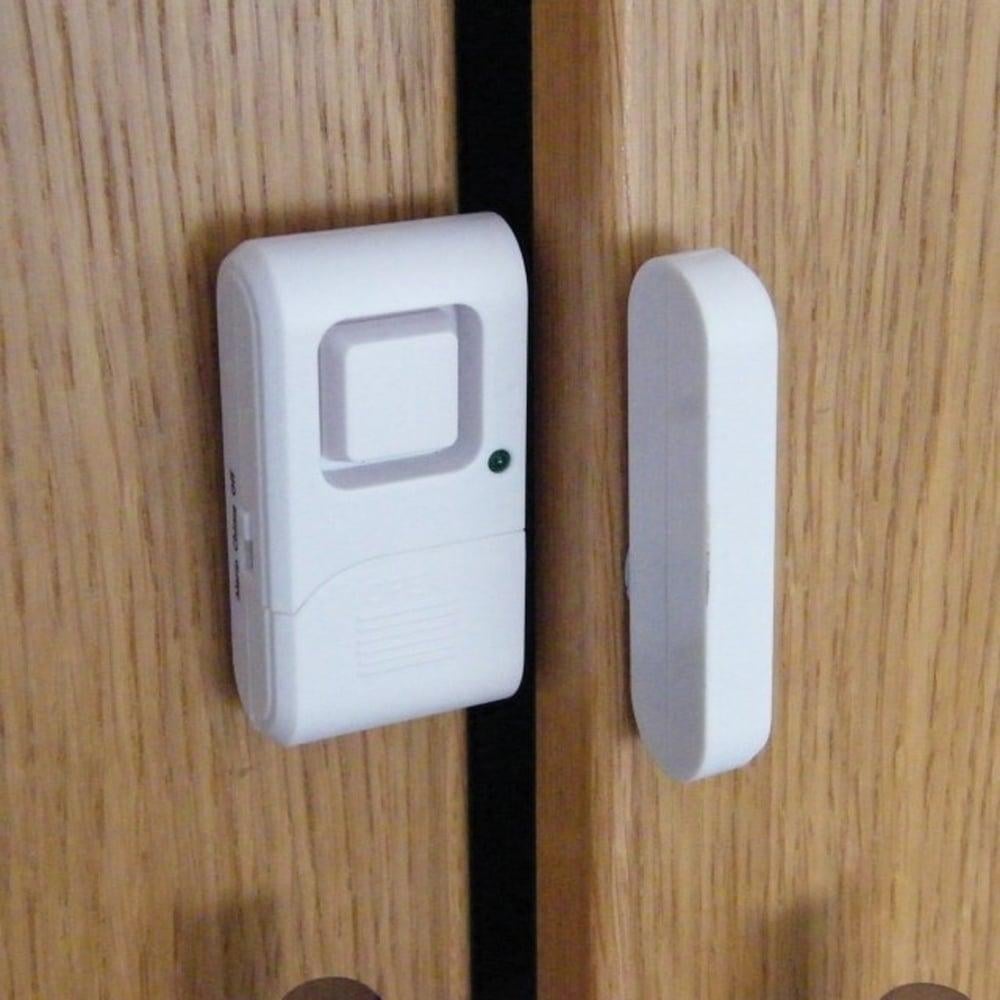 A white door alarm device mounted on a wooden door, with a magnetic sensor stick attached.