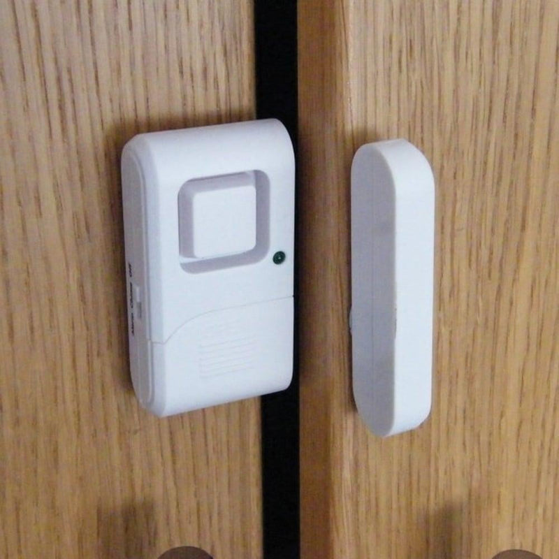 A white door chime and alarm device mounted on a wooden door, with a magnetic sensor stick attached.